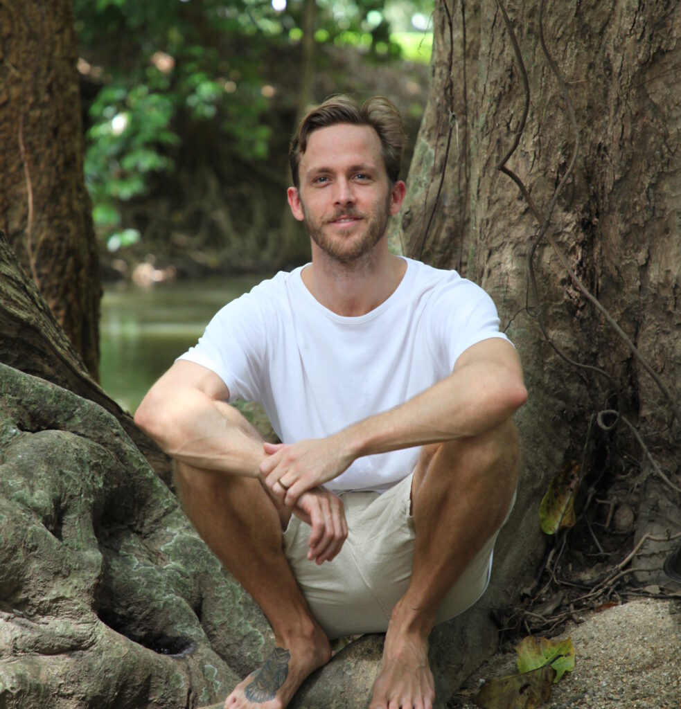Campbell Will sitting against large tree roots near water